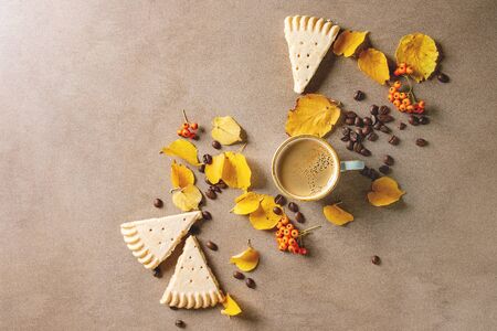 Cup of espresso coffee with yellow autumn leaves, berries, coffee beans and shortbread cookies over brown texture background. Fall concept. Flat lay, spaceの写真素材