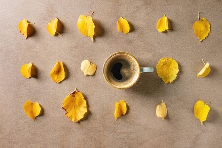 Cup of espresso coffee with yellow autumn leaves in row over brown texture background. Fall concept. Flat lay, spaceの写真素材