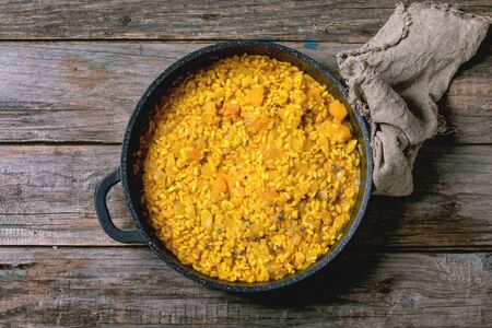 Traditional vegetarian pumpkin risotto italian dish in iron pan with cloth rag over old wooden background above. Flat lay, spaceの写真素材