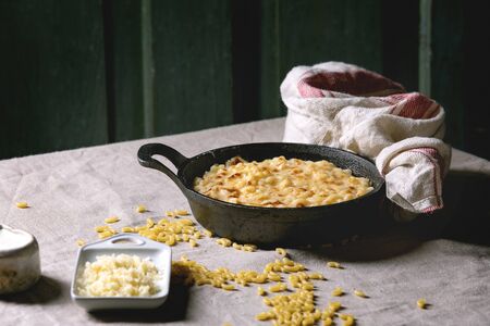Classic american dish baked mac and cheese in cast iron pan with kitchen towel and ingredients above...