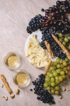 Swiss cheese tete de moine on ceramic board, black and green grapes and two glasses of white wine, served with bread sticks on pink marble background. Flat lay, spaceの写真素材
