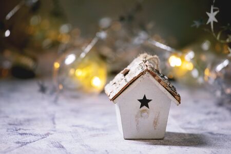 Christmas toy birdhouse and lightning garlands over old white wooden background. Christmas and New year decorations or greeting card. Copy spaceの写真素材