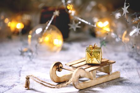 Christmas wood toys sled with gift boxes and lightning garlands over old white wooden table. Christmas and New year decorations or greeting card.の写真素材