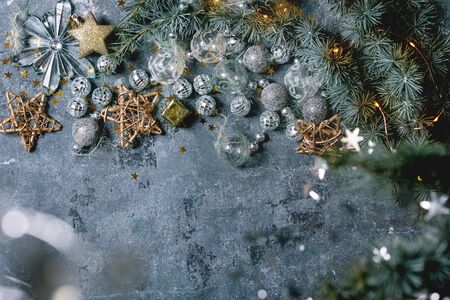 Variety of Christmas toys, silver balls and lighted garlands on fir tree branches over blue texture background. Flat lay, space. Christmas and New year decorations or greeting card.の写真素材