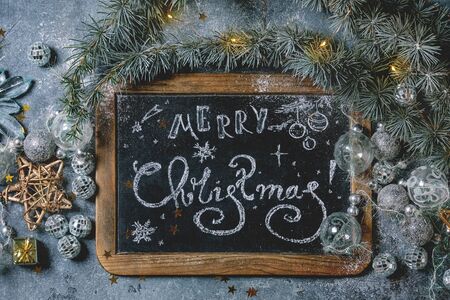 Christmas hand lettering Merry Christmas on vintage chalkboard with fir tree, golden stars, toys and lighted garland over blue texture background. Flat lay, spaceの写真素材