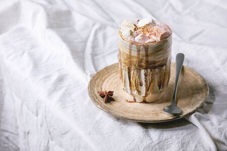 Hot chocolate or cocoa with marshmallow served in ceramic mug with saucer and spoon on white folded table cloth.の写真素材