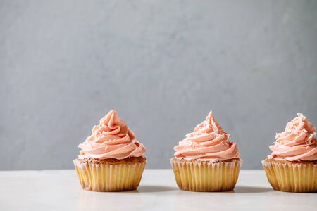 Homemade cupcakes with pink buttercream and coconut flakes in row on white marble table.の写真素材