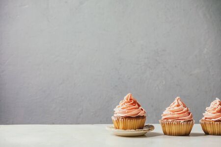 Homemade cupcakes with pink buttercream and coconut flakes in row on white marble table.の写真素材