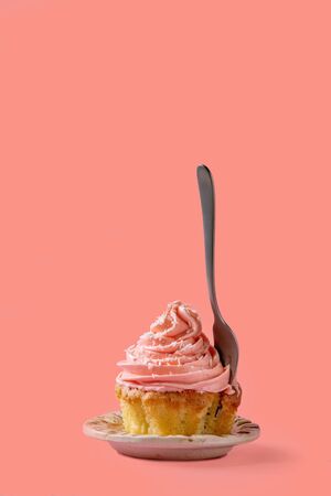 Homemade cupcake with pink buttercream and coconut flakes, with dessert fork within over red pink background.の写真素材