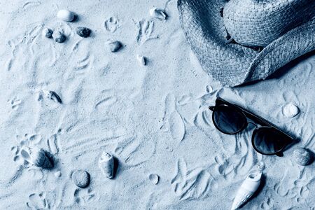 Summer theme. Shells, sea stones, sunglasses and straw hat on white sand as background. Flat lay. Color of the year 2020 classic blue tonedの写真素材