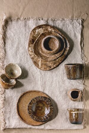 Variety of empty different handmade ceramic dishes, bowls, jugs and plates over grey linen cloth as background. Flat lay, spaceの写真素材