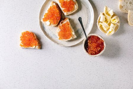 Red salmon caviar in bowl and on wheat bread, served with butter on ceramic plate over grey spotted background. Flat lay, spaceの写真素材