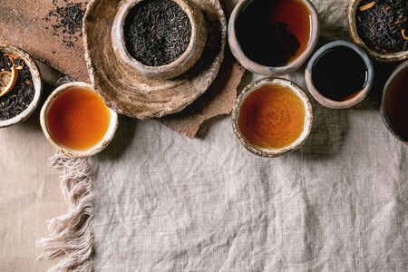 Variety of hot and dry tea green and black in traditional and wabi sabi style fireclay ceramic craft cups and bowls, served on linen cloth as background. Flat lay, spaceの写真素材