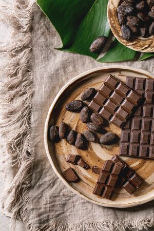 Dark and milk chocolate bar whole and chopped in ceramic plate with cocoa beans and cocoa powder on...