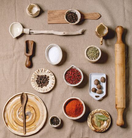 Variety of different handmade wooden and ceramic dishes, bowls and cutlery with seasonings and spices over grey linen cloth as background. Flat lay, space. Kitchen cooking conceptの写真素材