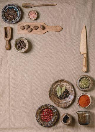 Variety of different handmade wooden and ceramic dishes, bowls and cutlery with seasonings and spices over grey linen cloth as background. Flat lay, space. Kitchen cooking conceptの写真素材