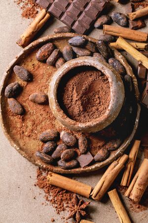 Dark and milk chocolate bar whole and chopped with cocoa beans, cocoa powder and cinnamon sticks over brown texture background. Flat lay, spaceの写真素材
