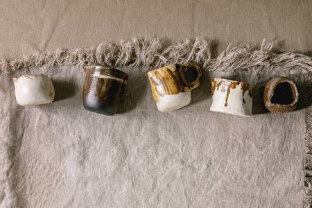 Variety of empty different handmade ceramic milc jugs over grey linen cloth as background. Flat lay, spaceの写真素材