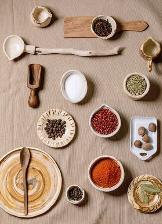 Variety of different handmade wooden and ceramic dishes, bowls and cutlery with seasonings and spices over grey linen cloth as background. Flat lay, space. Kitchen cooking conceptの写真素材