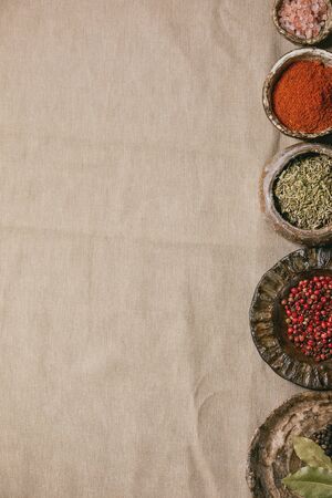 Variety of different handmade ceramic plates and bowls in row with seasonings and spices over grey linen cloth as background. Flat lay, copy space. Kitchen cooking conceptの写真素材