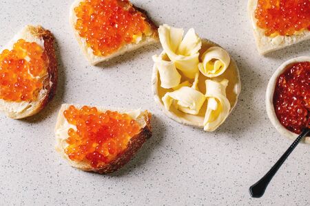 Red salmon caviar in bowl and on wheat bread, served with butter on ceramic plate over grey spotted background. Flat lay, spaceの写真素材