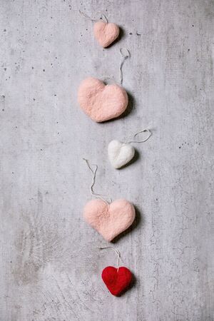 Variety of needle felted hearts on threads in row over grey texture background. Flat lay, copy space. St Valentines day greeting cardの写真素材