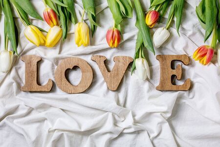 Wooden decorative letters word LOVE with colorful tulips over folded cotton cloth. Flat lay, space. Spring mood, st Valentines day gift cardの写真素材