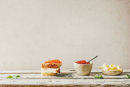 Red salmon caviar in ceramic bowl and on wheat bread, served with butter on old wooden table. Rustic...