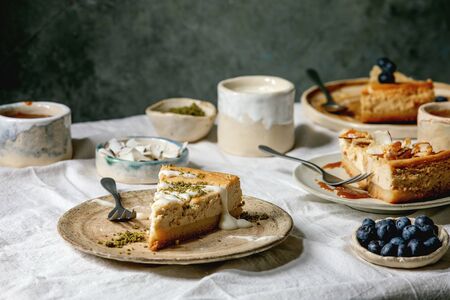 Pieces of cheesecake with different toppings on ceramic plates and variety of sauces in ceramic...