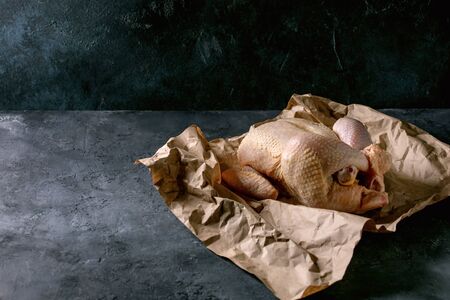 Whole raw organic uncooked farmer chicken poultry on crumpled craft paper over black concrete background. Copy spaceの写真素材