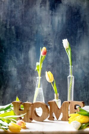 Wooden decorative letters word HOME with colorful tulips on white marble table with dark blue wall behind. Spring home decoration.の写真素材