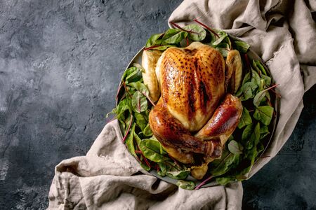 Whole baked chicken poultry on ceramic plate, served with green beetroot salad leaves on linen cloth over black concrete background. Flat lay, space. Dinner menuの写真素材