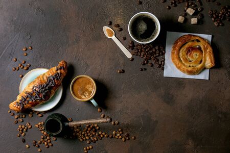 Variety of traditional french puff pastry raisin and chocolate buns, croissant with various cups of coffee and milk, cezve, recycled wooden spoon of sugar over dark texture background. Flat lay, spaceの写真素材