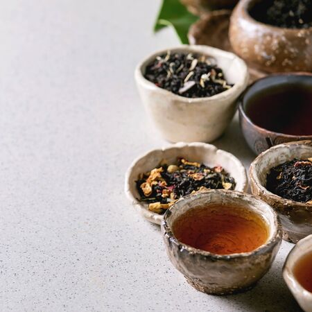 Variety of hot and dry tea green and black in traditional and wabi sabi style fireclay ceramic craft cups and bowls over grey spotted background. Close up, copy spaceの写真素材