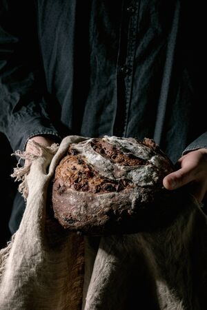 Man in black shirt holding in hands fresh baked artisan round homemade chocolate and cranberries rye...