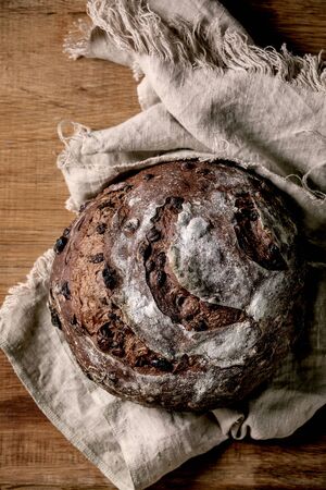Whole fresh baked artisan round homemade chocolate and cranberries rye bread on linen cloth over wooden table background. Flat lay, spaceの写真素材
