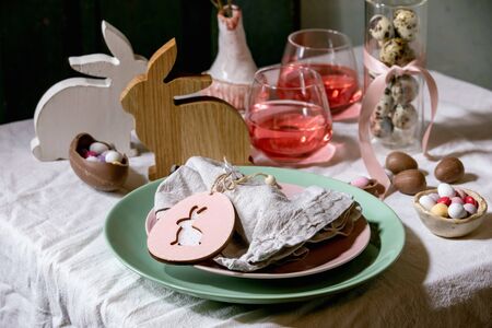 Easter table setting with wooden rabbit decoration, chocolate eggs and sweets, glasses of pink...