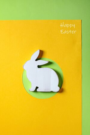 Easter minimal greeting card with white wooden rabbit decoration on bright paper yellow green background. Happy Easter inscription. Flat lay, copy space.の写真素材