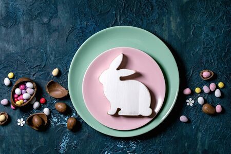 Easter table setting with chocolate eggs, candies and empty plates with wooden Easter decoration...