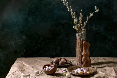 Easter mood still life with blossom willow branches in ceramic vase, traditional chocolate rabbit,...