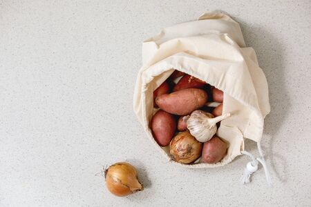 Variety of fresh organic vegetables potatoes, onion and garlic in white cotton shopping bag. Eco friendly, zero waste. Grey texture background.の写真素材