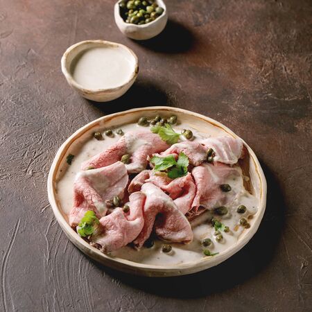 Vitello tonnato italian dish. Thin sliced veal with tuna sauce, capers and coriander served on ceramic plate over dark texture background.の写真素材