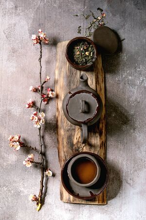 Tea drinking wabi sabi japanese style dark clay cup and teapot on wooden board with blooming cherry branches. Grey texture concrete background. Flat lay, spaceの写真素材
