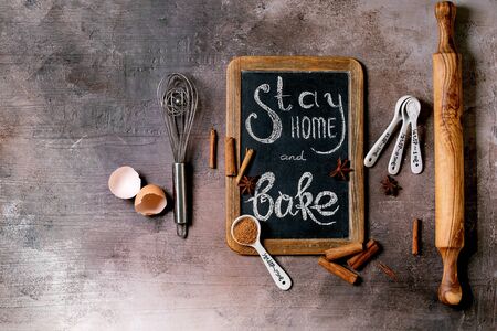 Ingredients and tools for baking. Stay home quarantine isolation period concept. Vintage chalkboard with handwritten chalk lettering Stay home and bake. Grey texture background. Flat lay, spaceの写真素材
