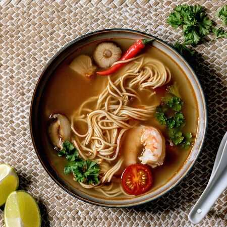 Asian spicy noodles soup with shiitake mushrooms and prawns, ingredients above on straw wicker napkin as background. Flat lay, space. Asian style dinnerの写真素材
