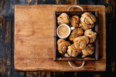 Traditional Swedish cardamom or cinnamon sweet buns Kanelbulle in wooden tray, cup of coffee on wooden table. Flat lay, spaceの写真素材
