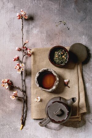 Tea drinking wabi sabi japanese style dark clay cups and teapot on cloth napkin with blooming cherry branches. Grey texture concrete background. Flat lay, spaceの写真素材