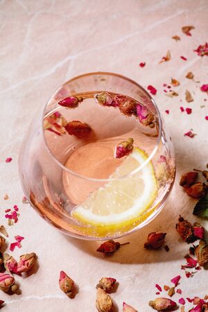 Cocktail glasses of pink rose champagne, cider or lemonade with dry rose buds and lemon. Pink marble background. Close upの写真素材