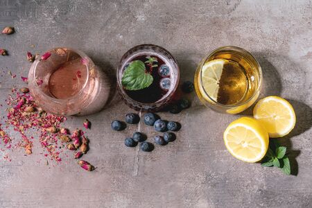 Different cocktail glasses with sparkling colorful drinks pink rose champagne, cider or lemonade with dry rose buds, lemon, blueberries and mint. Ingredients above. Texture background. Flat lay, spaceの写真素材