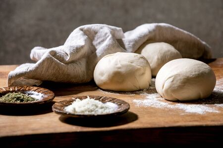 Dough for italian pizza napolitana cooking. Three balls of fresh homemade wheat dough and ingredients in ceramic plates above on wooden kitchen table. Home baking.の写真素材